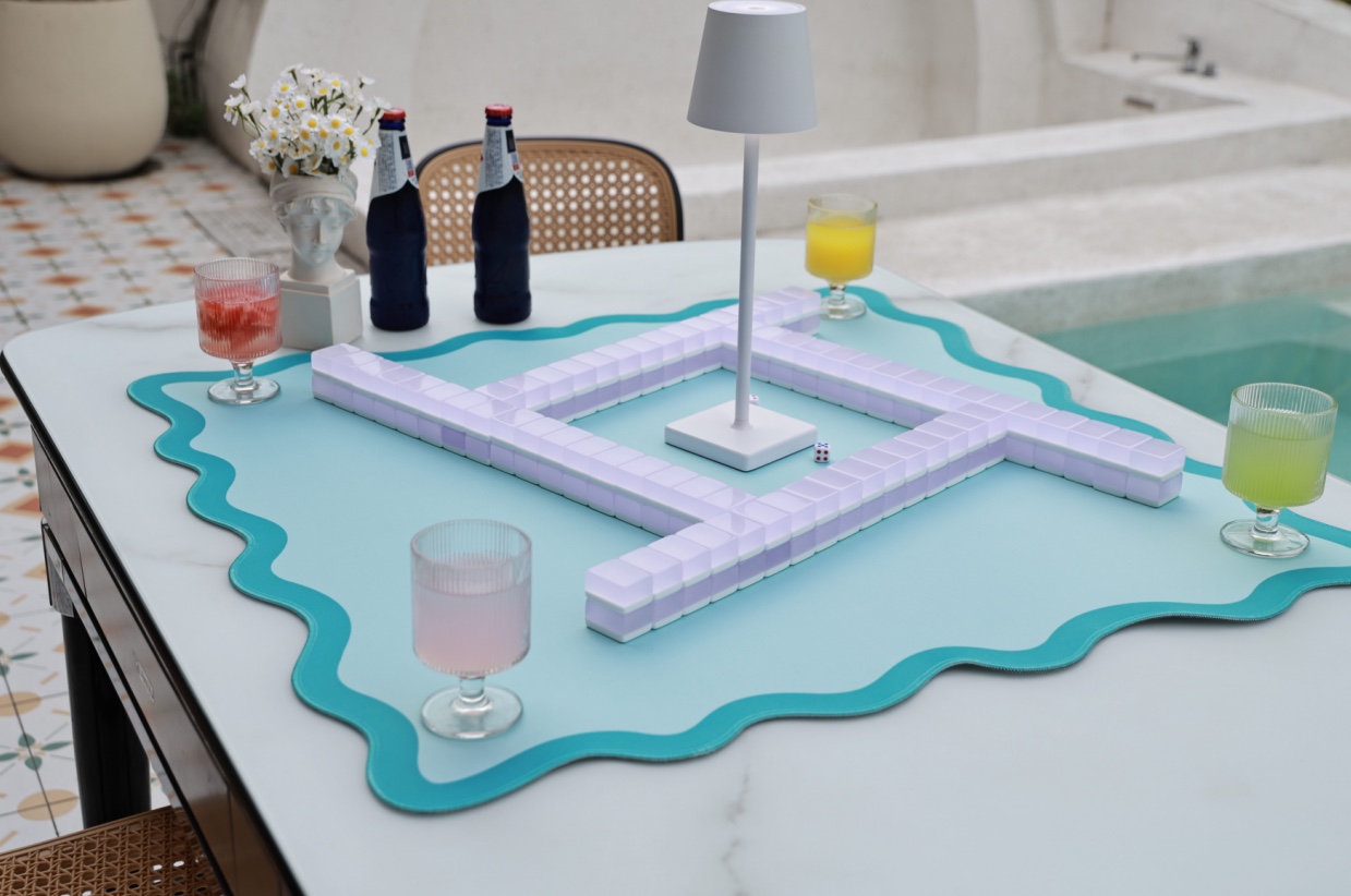 The green aknonr scalloped mat on a white marble table by a pool, with a game of mahjong set up on it